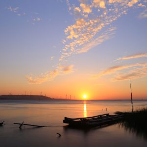 Beautiful sunrise over a lake featuring a wooden boat and distant windmills under a vibrant sky.